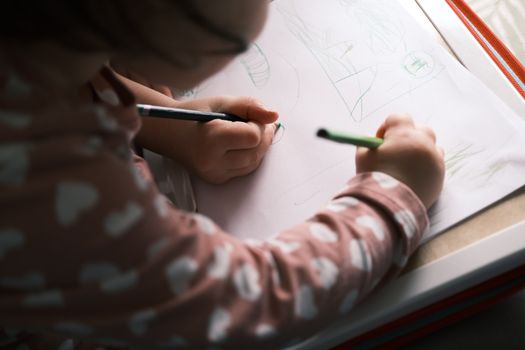 A young child drawing with colored pencils, capturing creativity and concentration in soft lighting indoors.