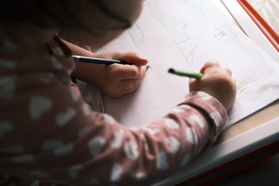 A young child drawing with colored pencils, capturing creativity and concentration in soft lighting indoors.