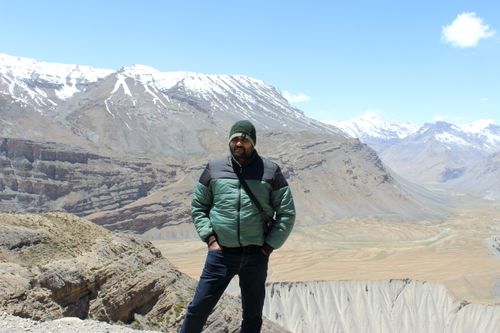 Free Man in green jacket posing in front of stunning snowy mountains under a clear blue sky. Stock Photo