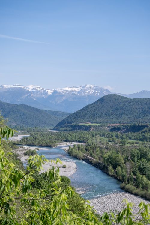 Free A tranquil river flows through a lush alpine valley with snow-capped peaks in the distance. Stock Photo