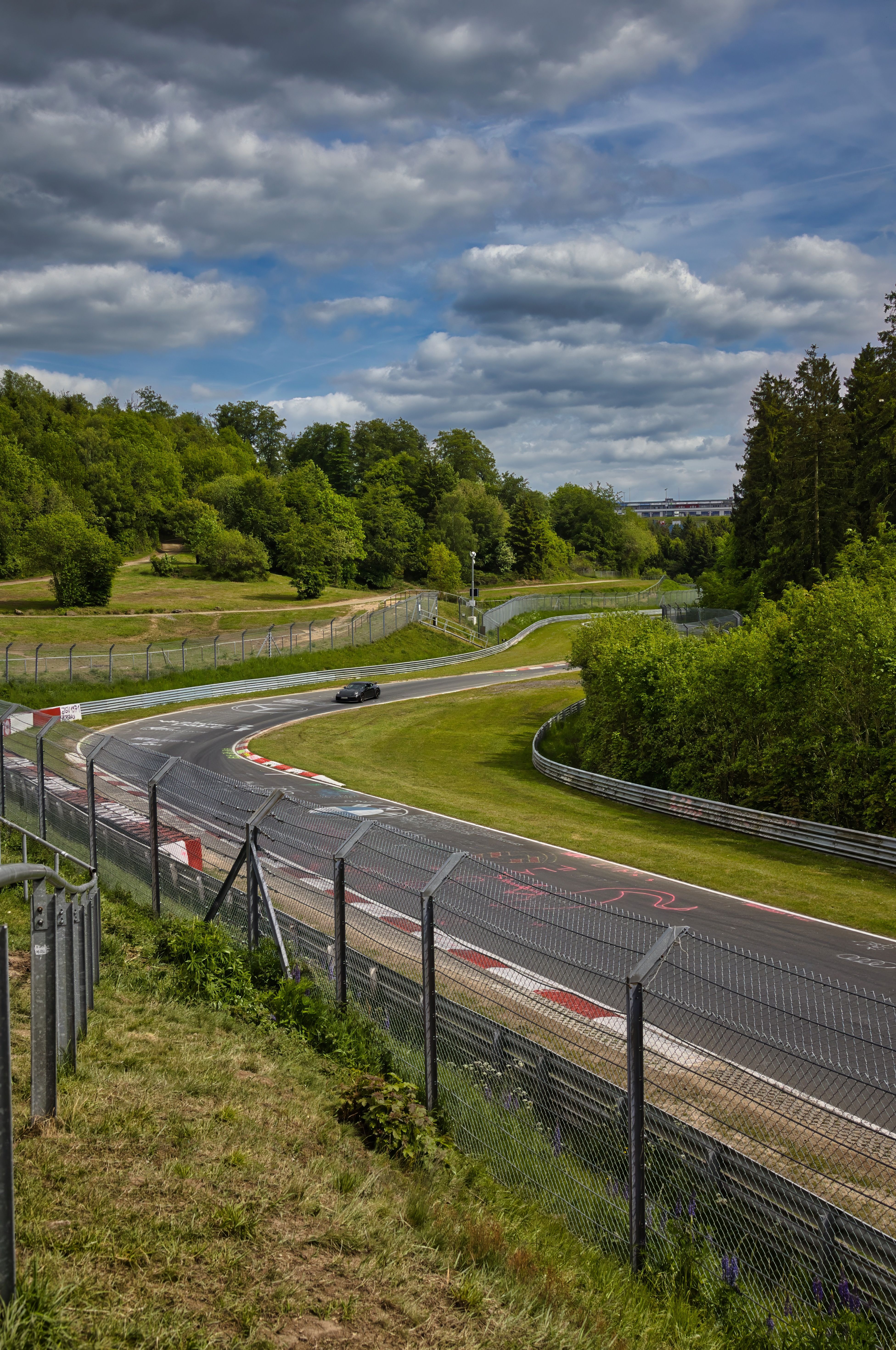 A picturesque view of the famous Nürburgring racing track surrounded by lush greenery under a cloudy sky.