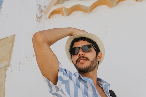 Hombre En Polo De Rayas Azules Y Blancas Con Gafas De Sol Negras Y Sombrero Marrón