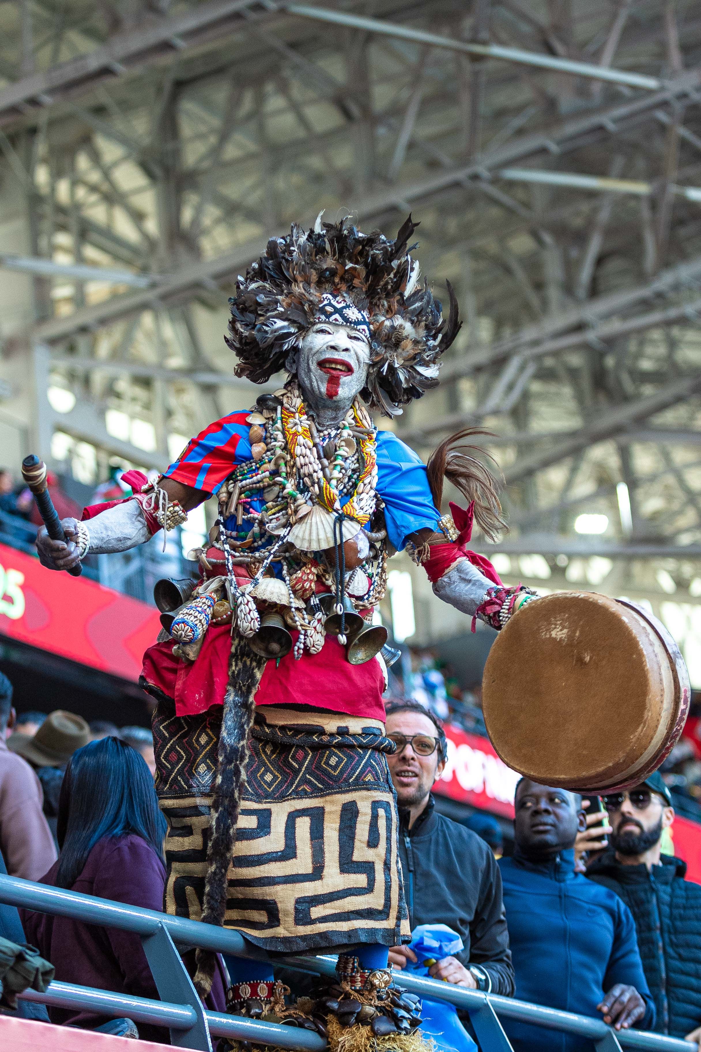 Tribal performer in colorful outfit and feathers entertains a stadium crowd.