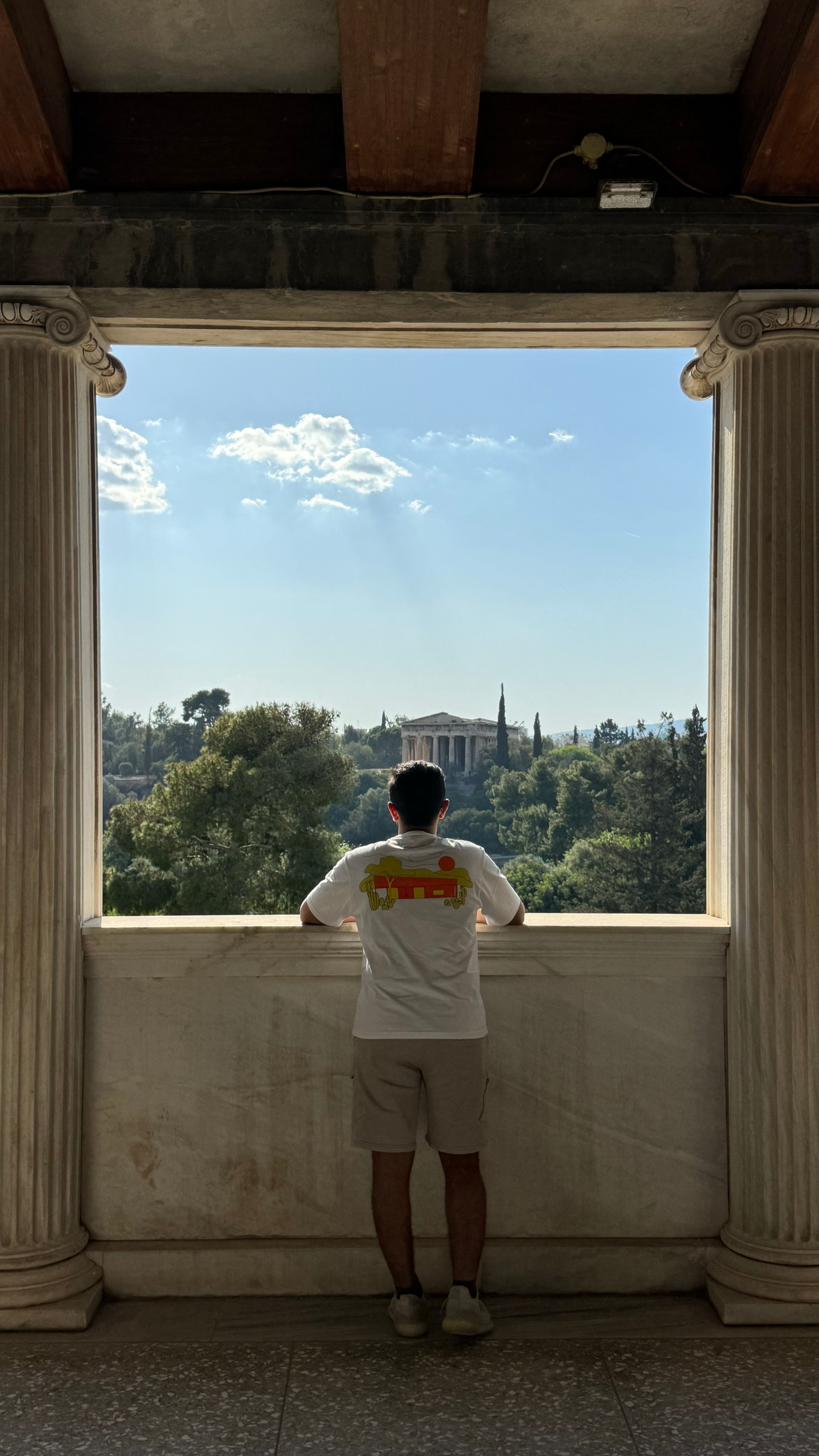 Man standing in Greek colonnade, viewing ancient temple in Athens.