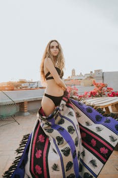 在墨西哥圣地亚哥德克雷塔罗的屋顶上，一名穿着泳装的女子被五颜六色的毯子裹住