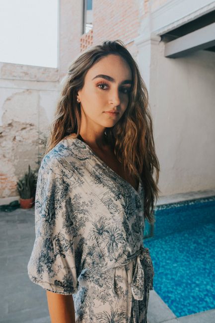 A young woman in a floral dress standing beside a pool, exuding elegance and confidence.