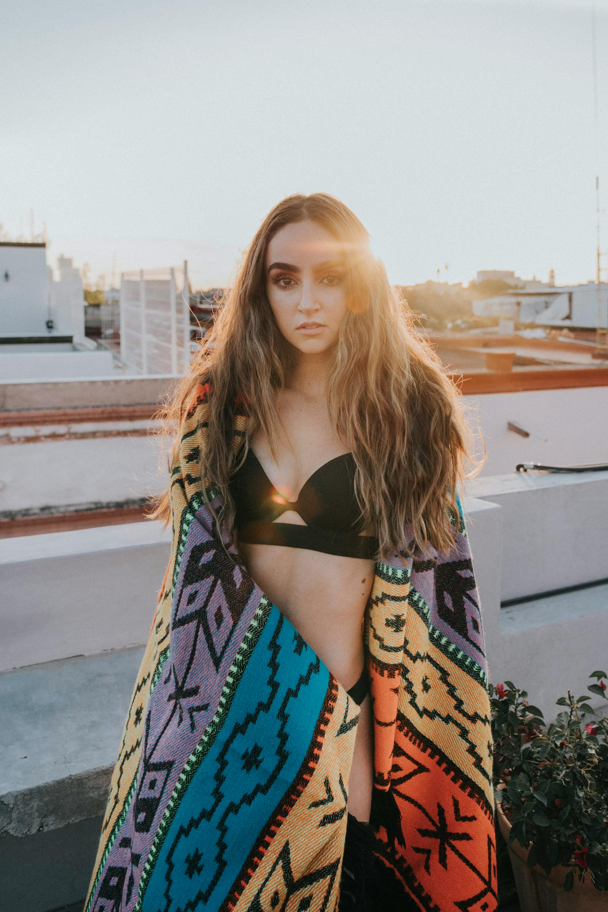 日落时分，屋顶上，一位身着黑色胸罩的女人裹着彩色毯子