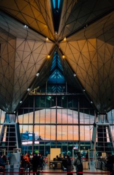 A modern airport terminal with stunning architectural design illuminated at sunset, depicting a busy scene with travelers.