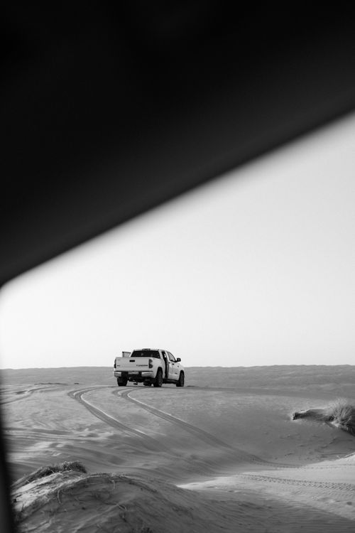 Free A monochrome photograph of a truck traversing sand dunes, showcasing solitude and adventure. Stock Photo