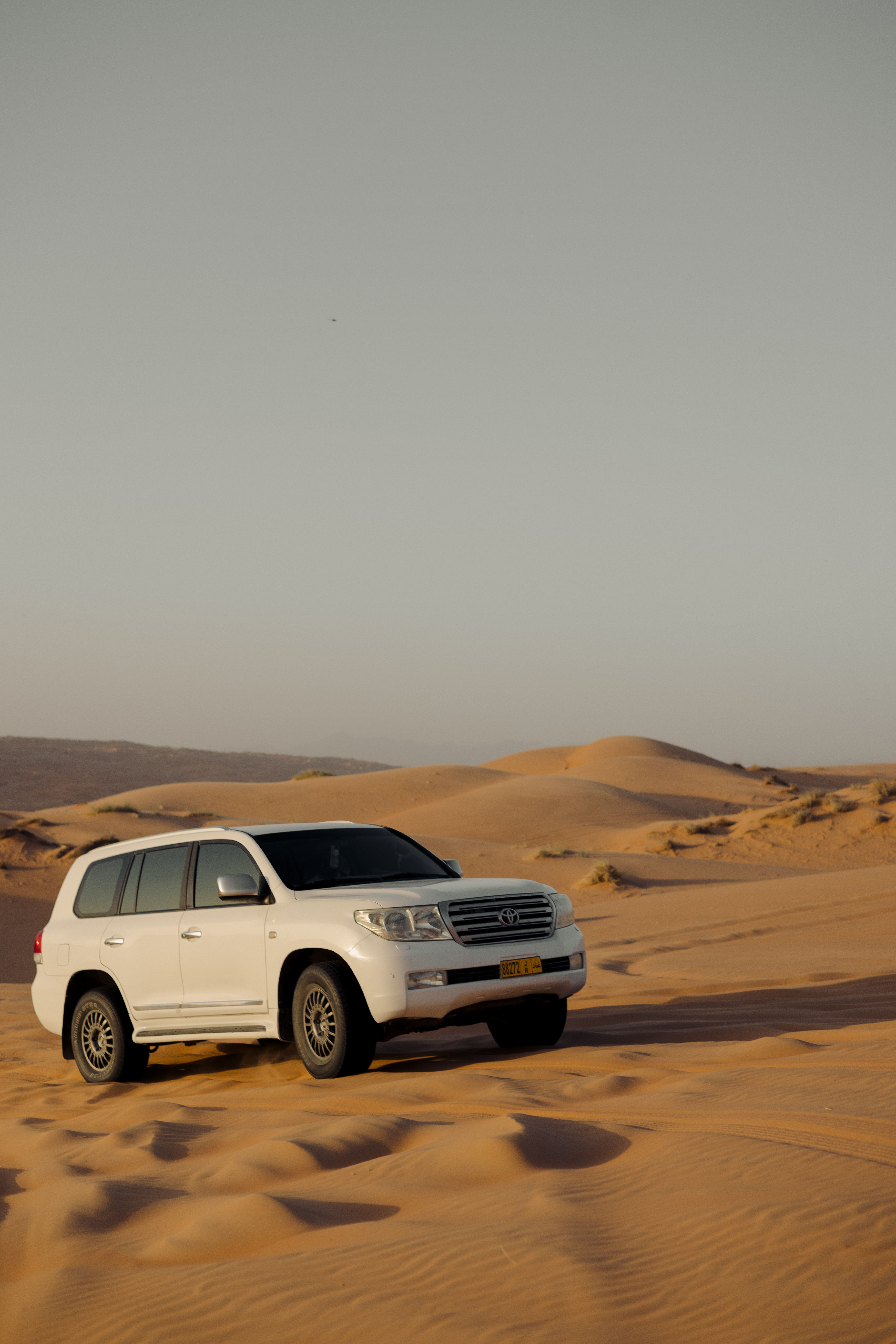 A white SUV navigates the expansive sand dunes of the Dubai desert under a clear sky.