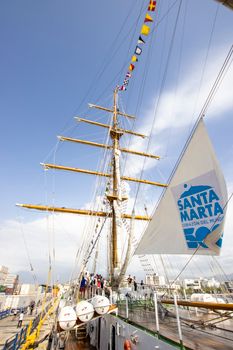 Tall ship with sails featuring "Santa Marta" branding docked in a sunny harbor.