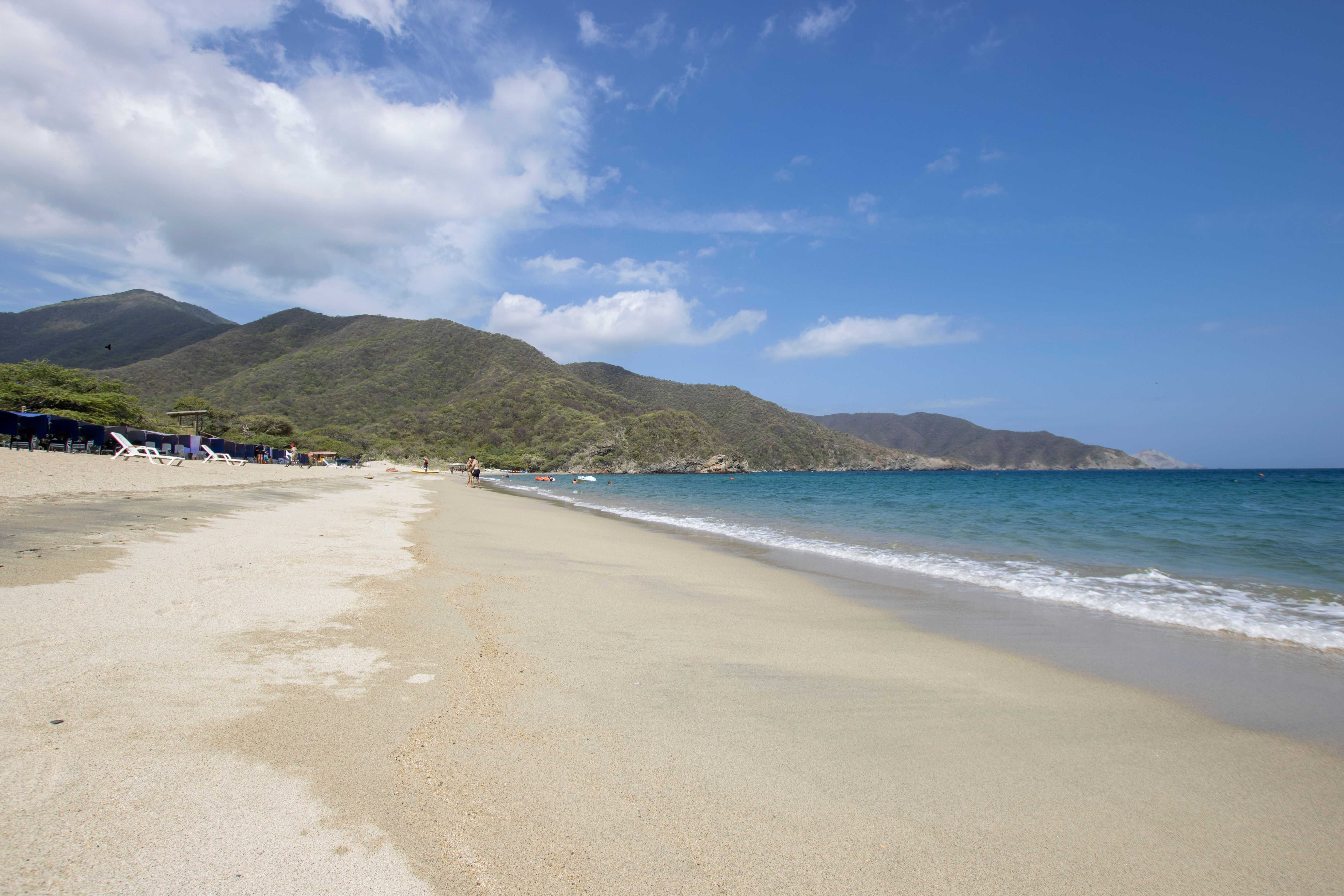 A serene beach scene featuring clear blue waters, sandy shores, and lush mountains in Tayrona National Park.