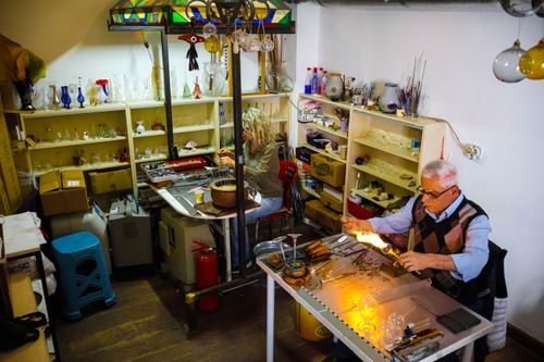 Free Artisans crafting glass pieces in a workshop with various tools and glass displays. Stock Photo