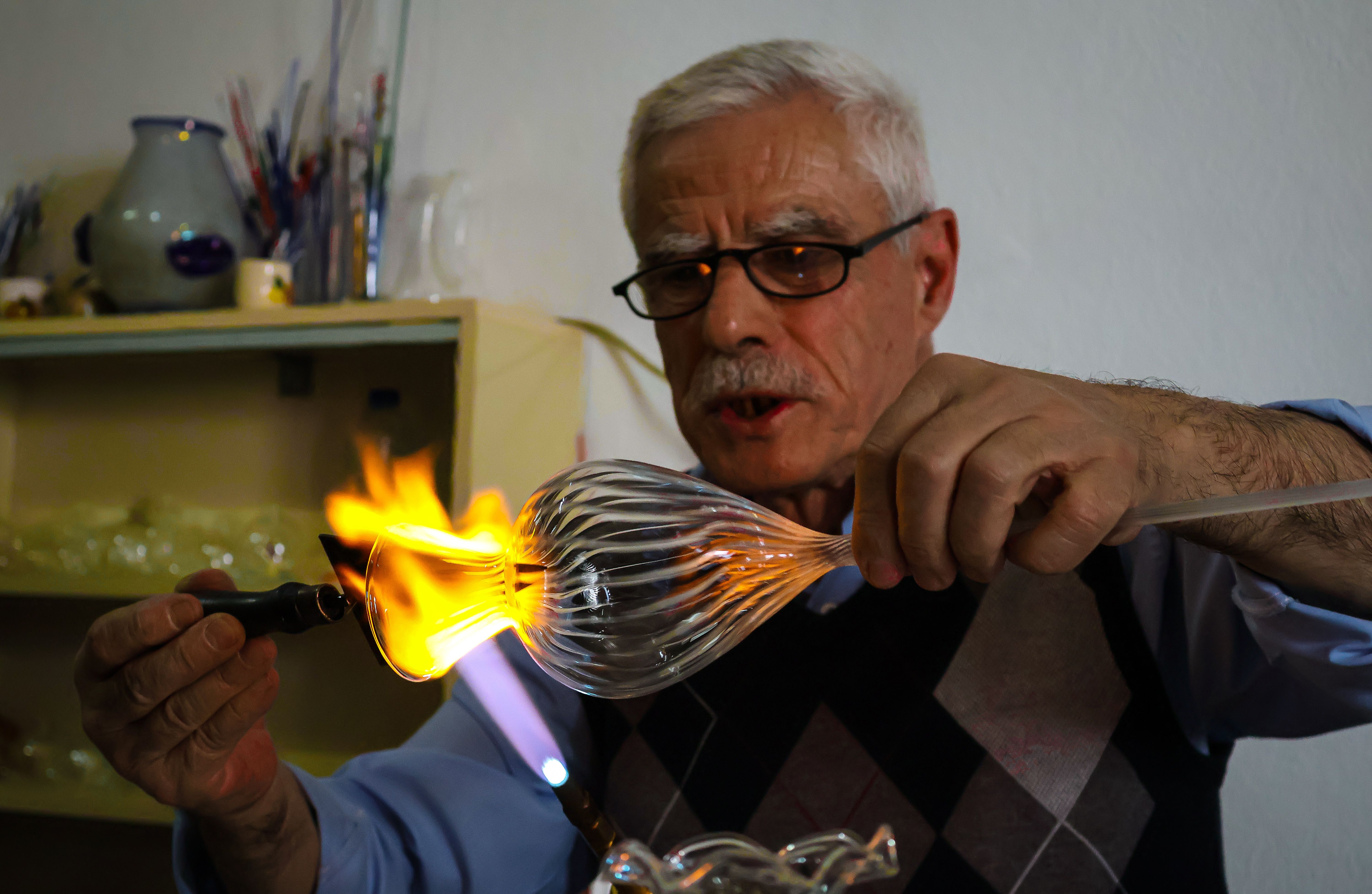 A skilled artisan blows glass with precision and flame, creating intricate designs in a studio setting.