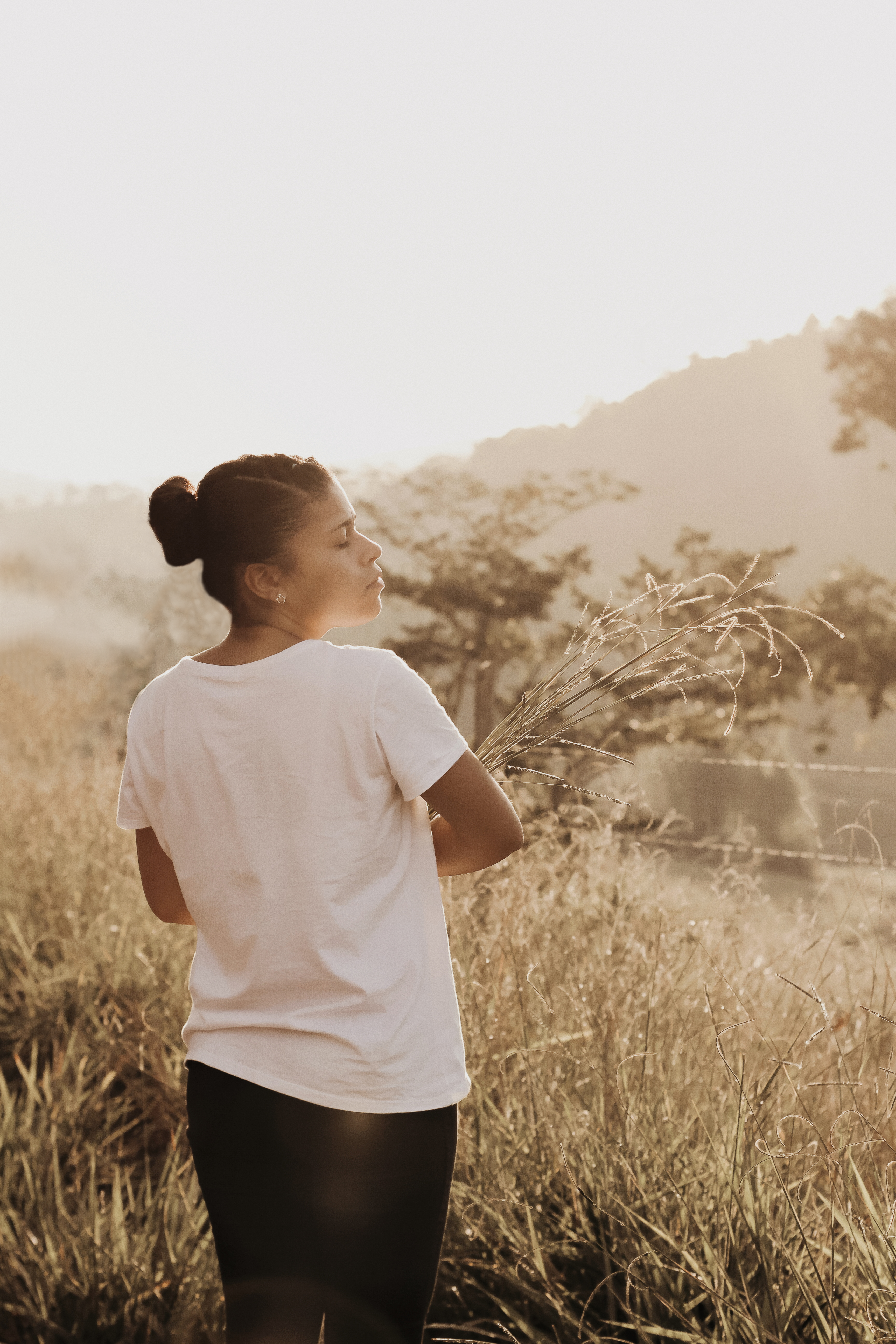 A serene woman stands in a sunlit grass field in Rio Vermelho, Brazil, embracing nature.