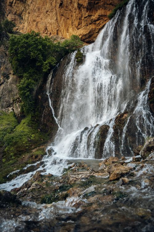 Free A beautiful waterfall cascading down rugged rocks surrounded by lush greenery. Stock Photo