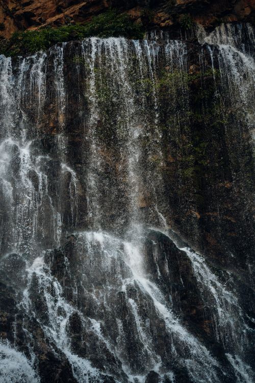Free A breathtaking waterfall cascading over rocks surrounded by lush greenery, captured in a natural outdoor setting. Stock Photo