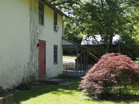 A rustic Pennsylvania home with a vibrant red door surrounded by lush greenery in summer.