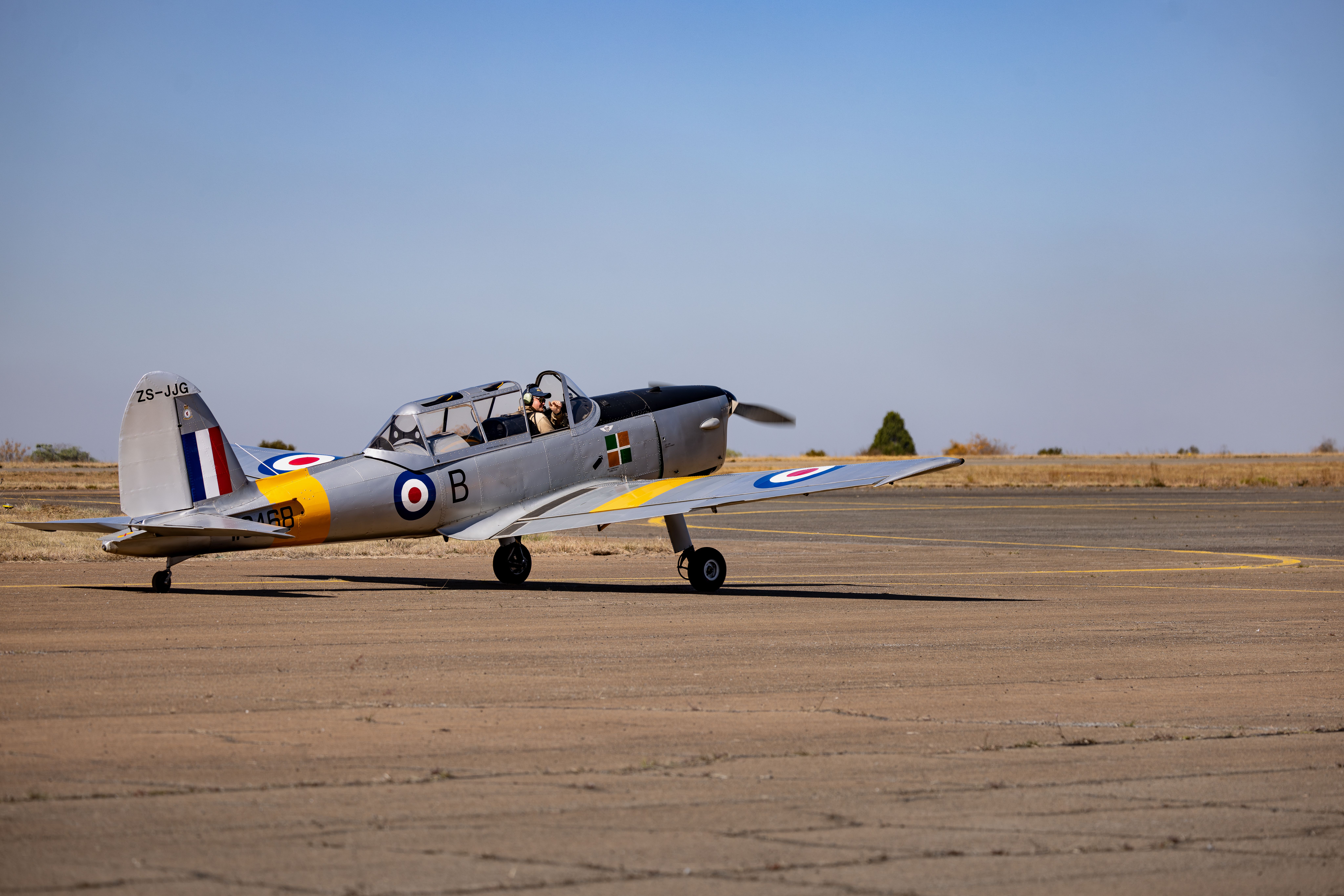 A vintage aircraft parked on a runway under a clear blue sky with a pilot preparing for takeoff.