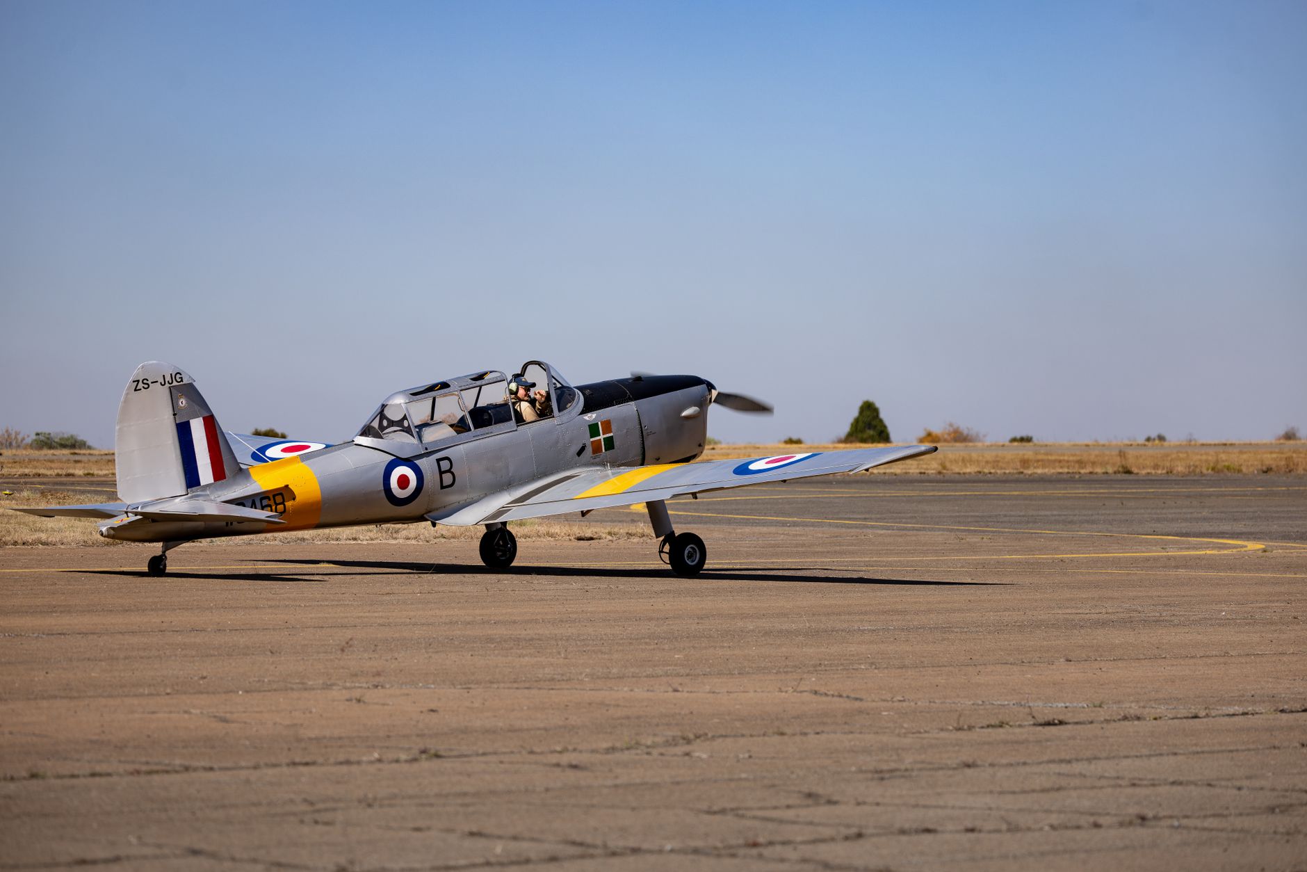 A vintage aircraft parked on a runway under a clear blue sky with a pilot preparing for takeoff.