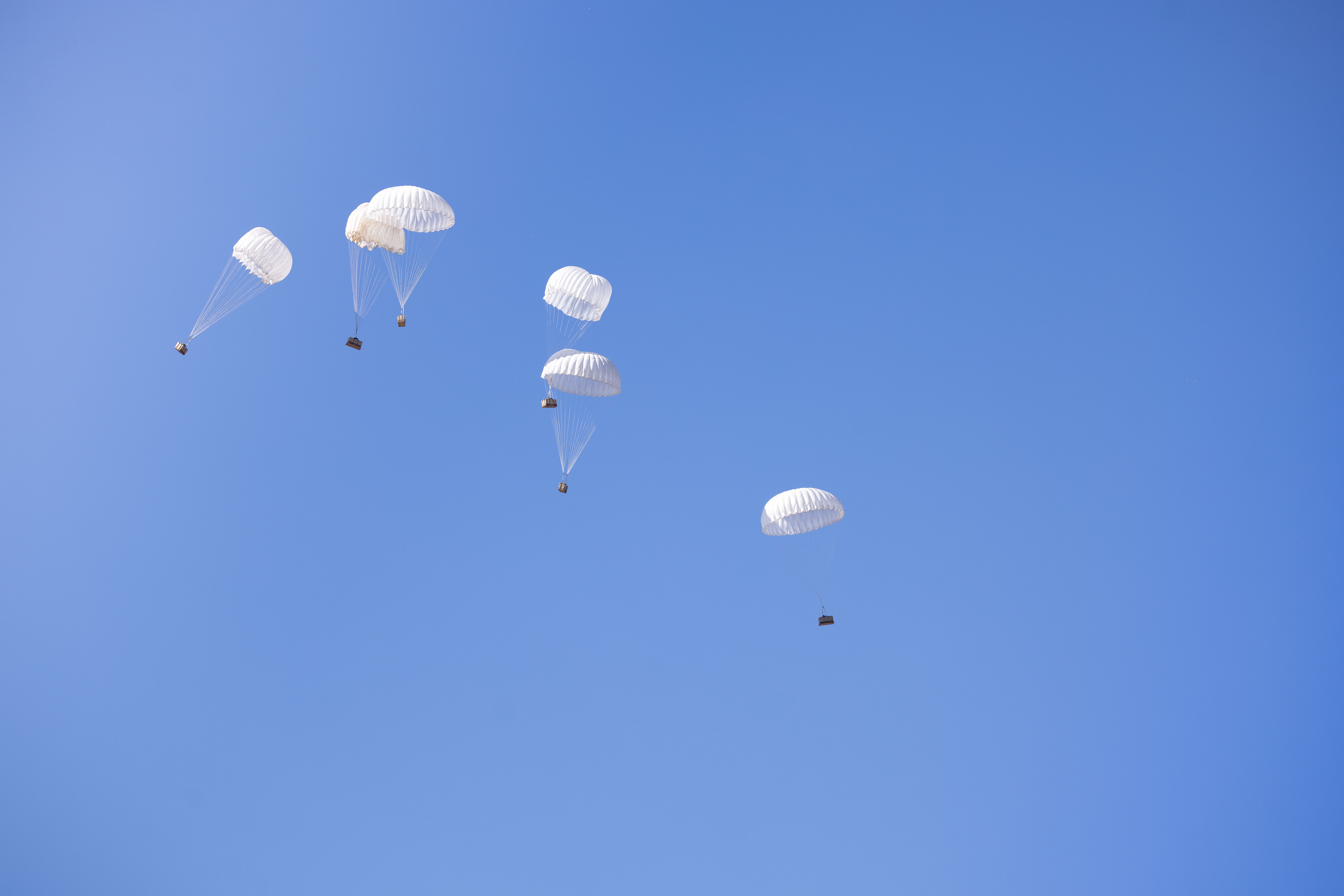 Multiple parachutes drop cargo boxes in a clear blue sky, showcasing aerial delivery technology.
