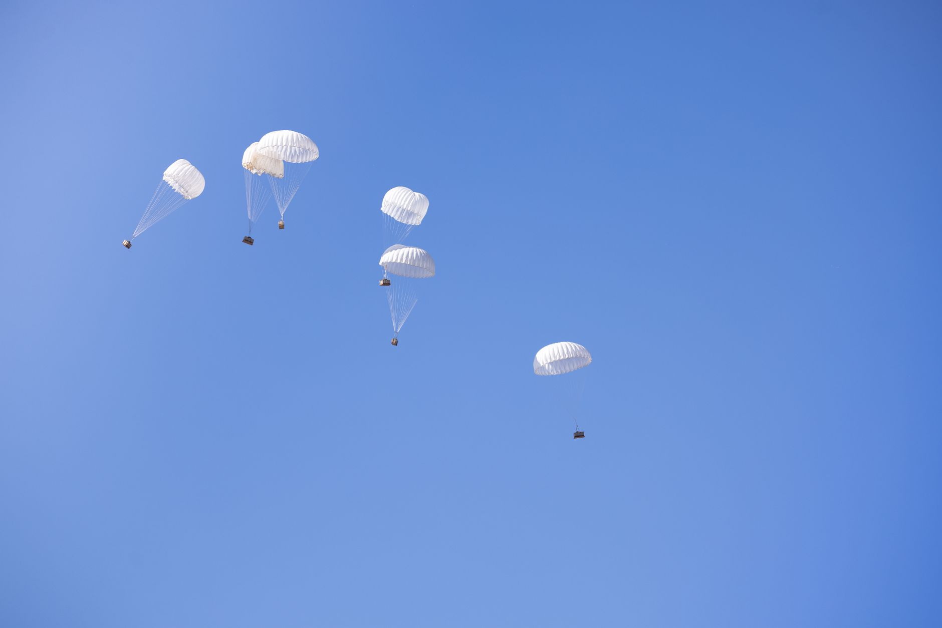Multiple parachutes drop cargo boxes in a clear blue sky, showcasing aerial delivery technology.