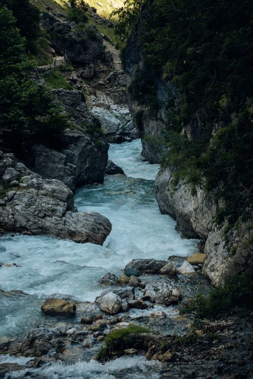 Free A picturesque view of a mountain stream flowing through a rocky gorge surrounded by lush greenery. Stock Photo