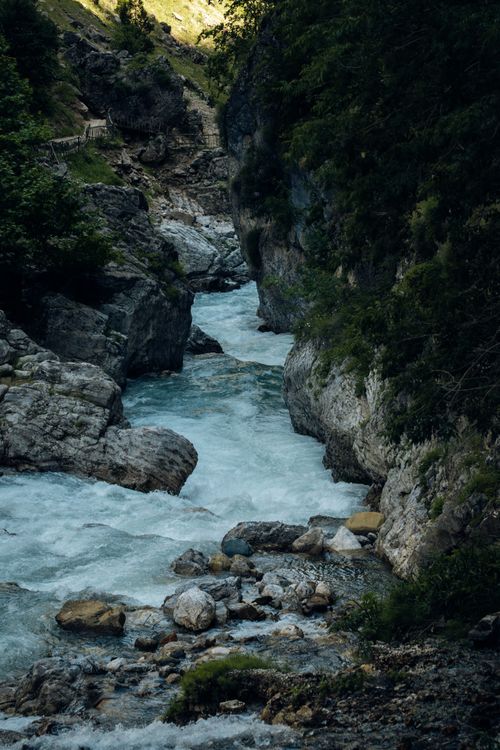 Free A picturesque mountain stream cascades through a rocky gorge surrounded by lush greenery, creating a serene nature scene. Stock Photo