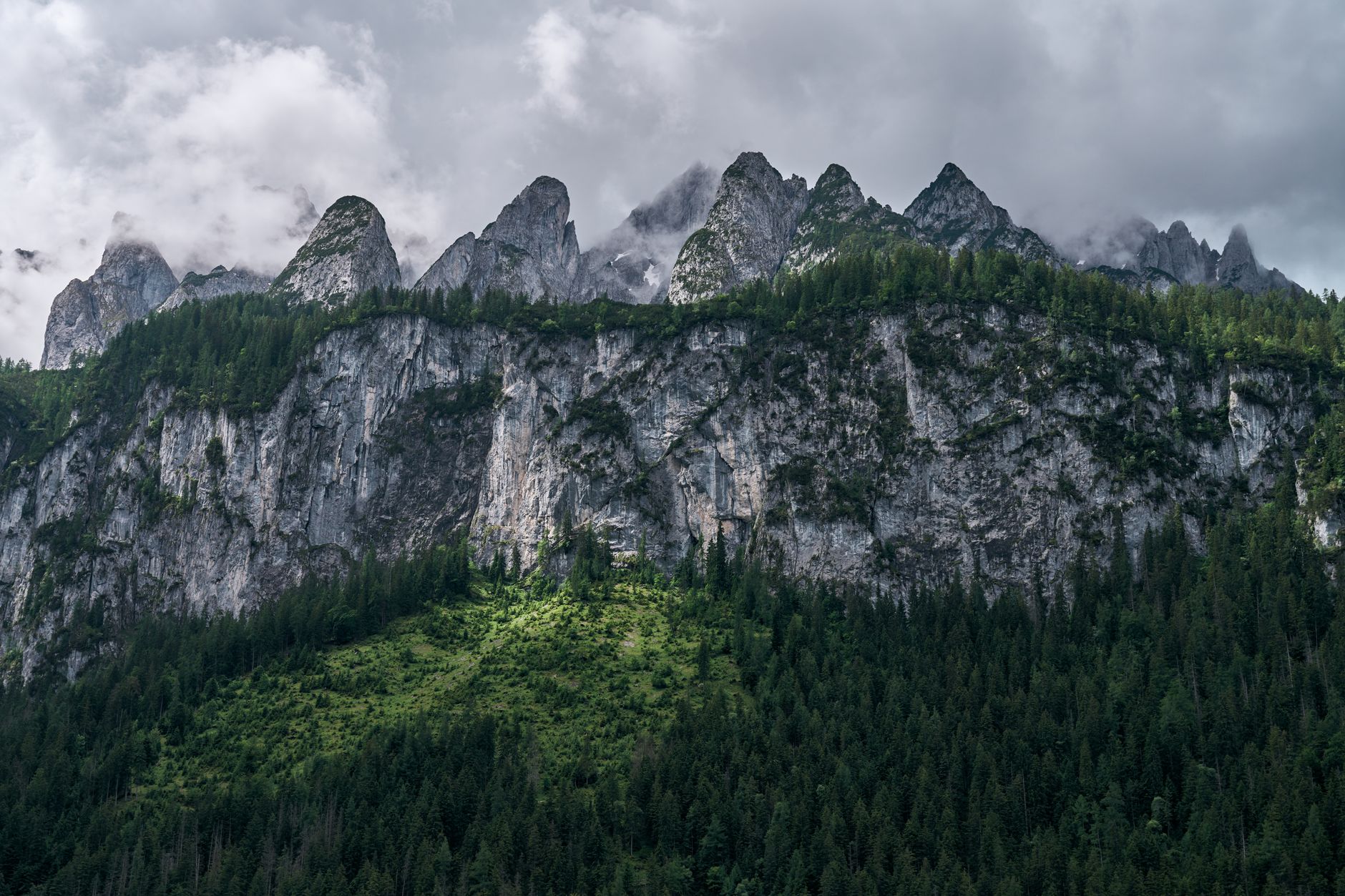 Majestic mountain range with lush forest under a cloudy sky, showcasing natural beauty and wilderness.