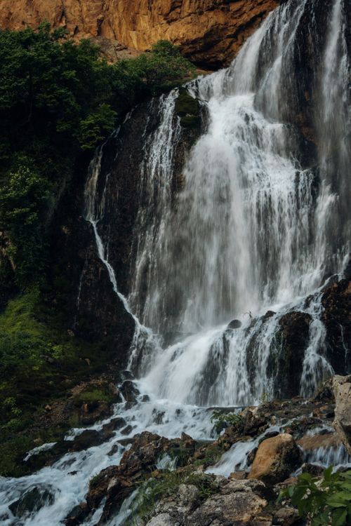 Free A stunning waterfall cascades down rocky cliffs surrounded by lush green forest, showcasing nature's beauty. Stock Photo