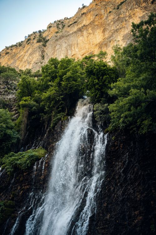 Free A stunning waterfall cascading down a rocky cliff surrounded by lush green foliage. Stock Photo