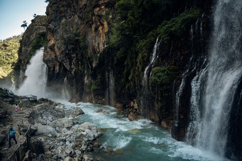 Free Breathtaking waterfall cascading down rocky cliffs along a lush mountain trail. Stock Photo