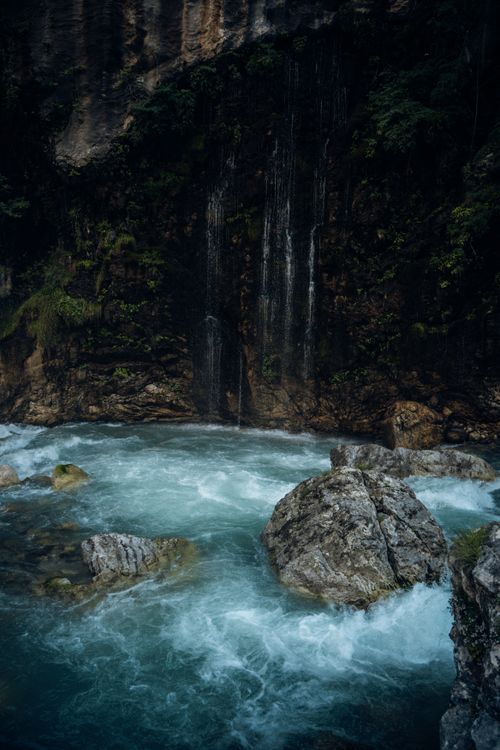 Free A tranquil waterfall cascading over lush rocks into a clear river, surrounded by verdant foliage. Stock Photo