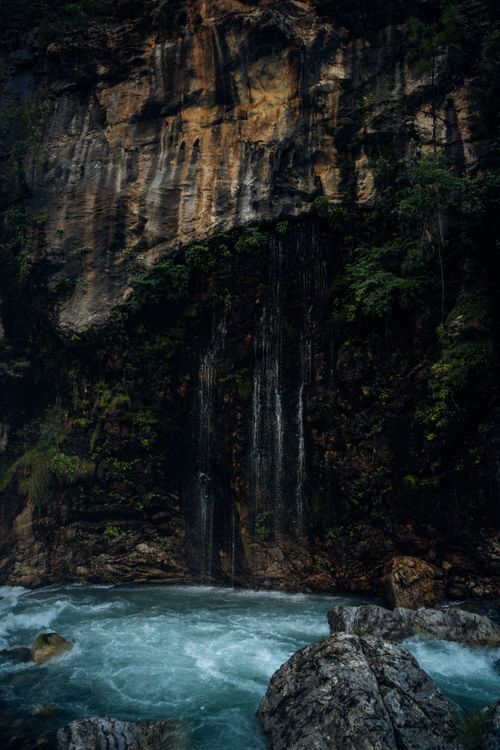 Free Stunning waterfall cascading down a rugged rock face into a blue pool, surrounded by greenery. Stock Photo