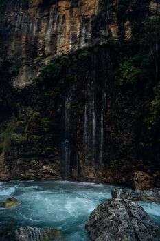 Peaceful waterfall cascading down rocky cliffs into a clear blue pool in a tranquil natural setting.