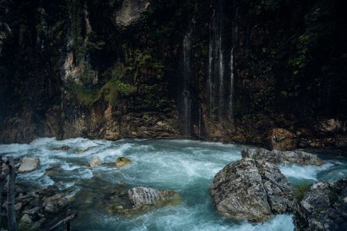 Free A tranquil waterfall cascading over rocky cliffs into a flowing river in a lush forest. Stock Photo