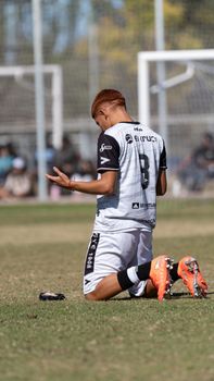 A young soccer player kneels on the field in a moment of prayer during a match.