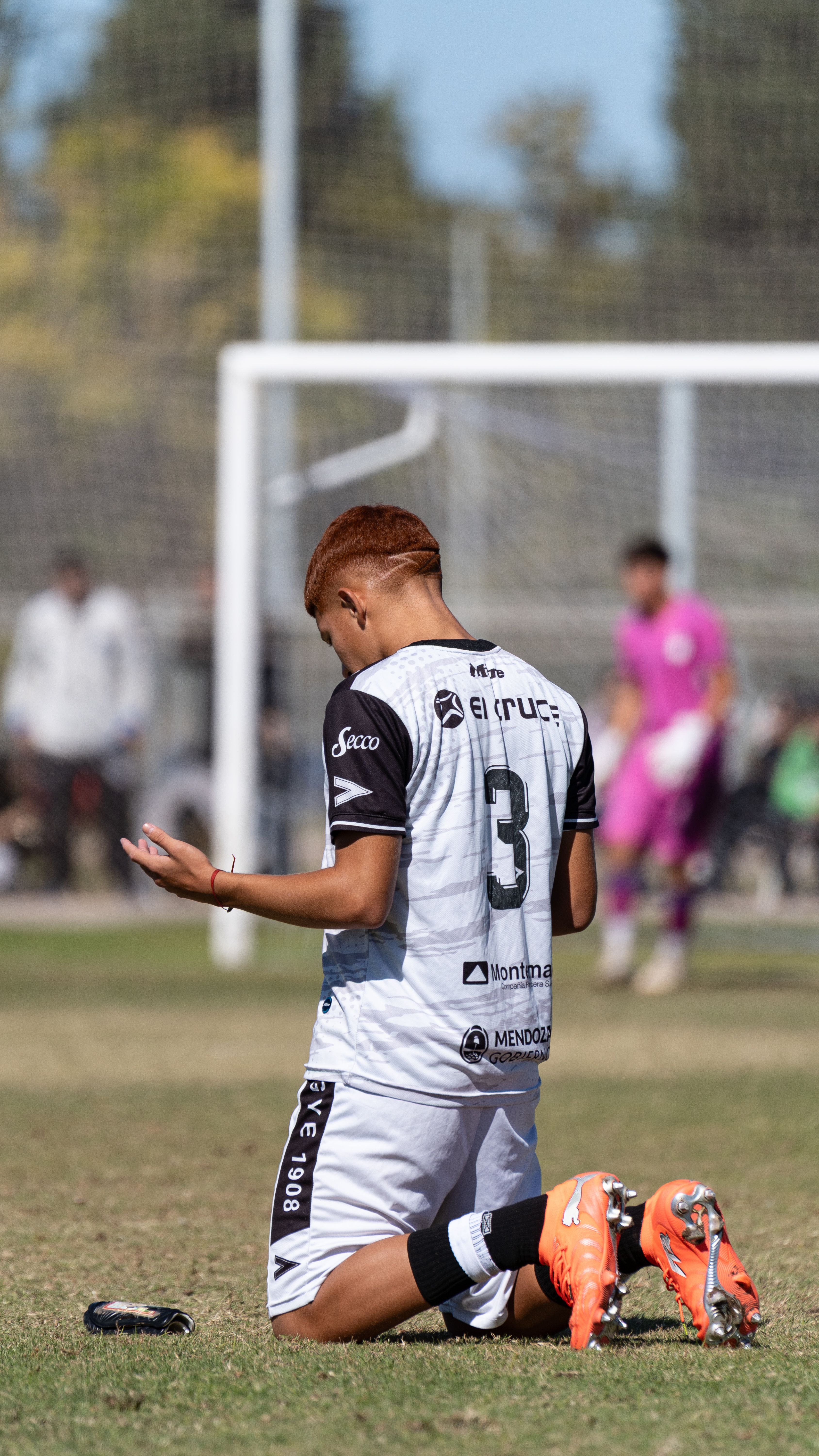 Soccer player kneeling on field in contemplation during a sunny day match.