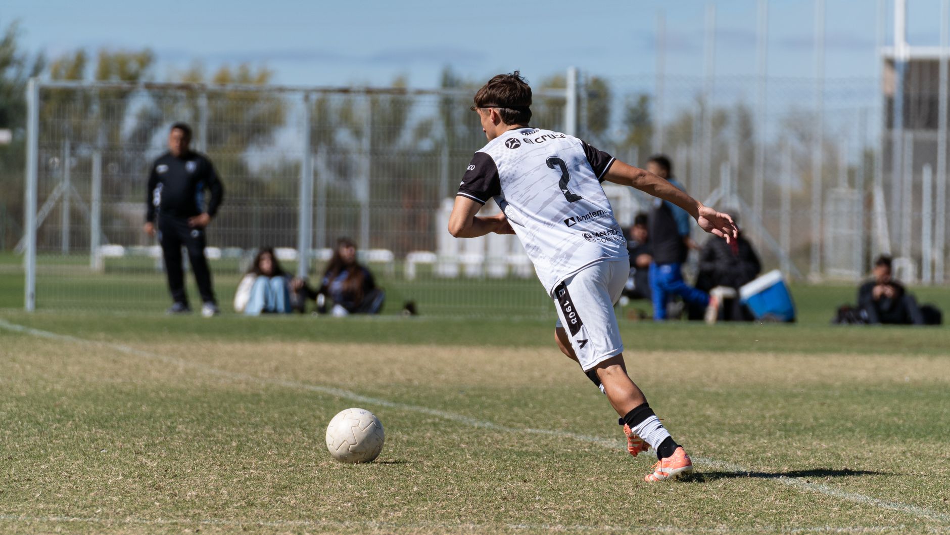 Teen soccer player preparing a kick during a match on a sunny day.