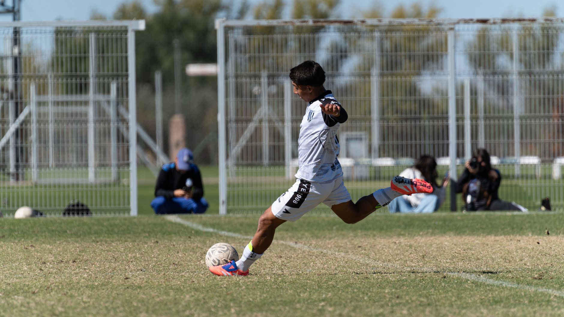 A youth football player performing close-control touches on a marked grass training pitch at sunrise