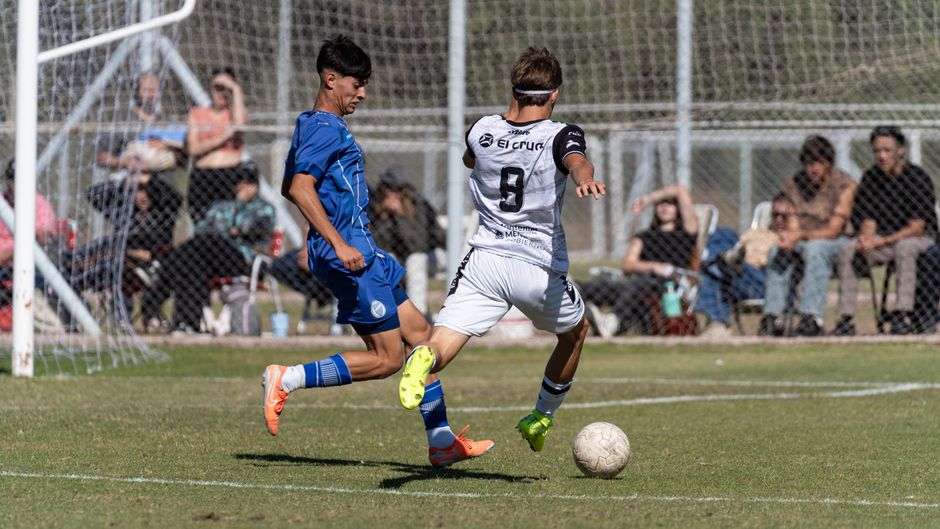 Intense soccer match with young players competing and spectators watching on a sunny day.