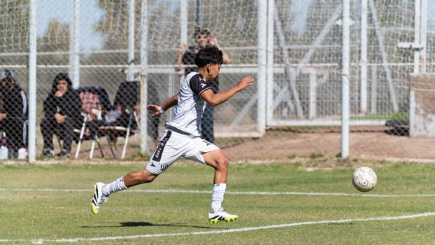 A dynamic image of a young male soccer player running and kicking a soccer ball during a game.