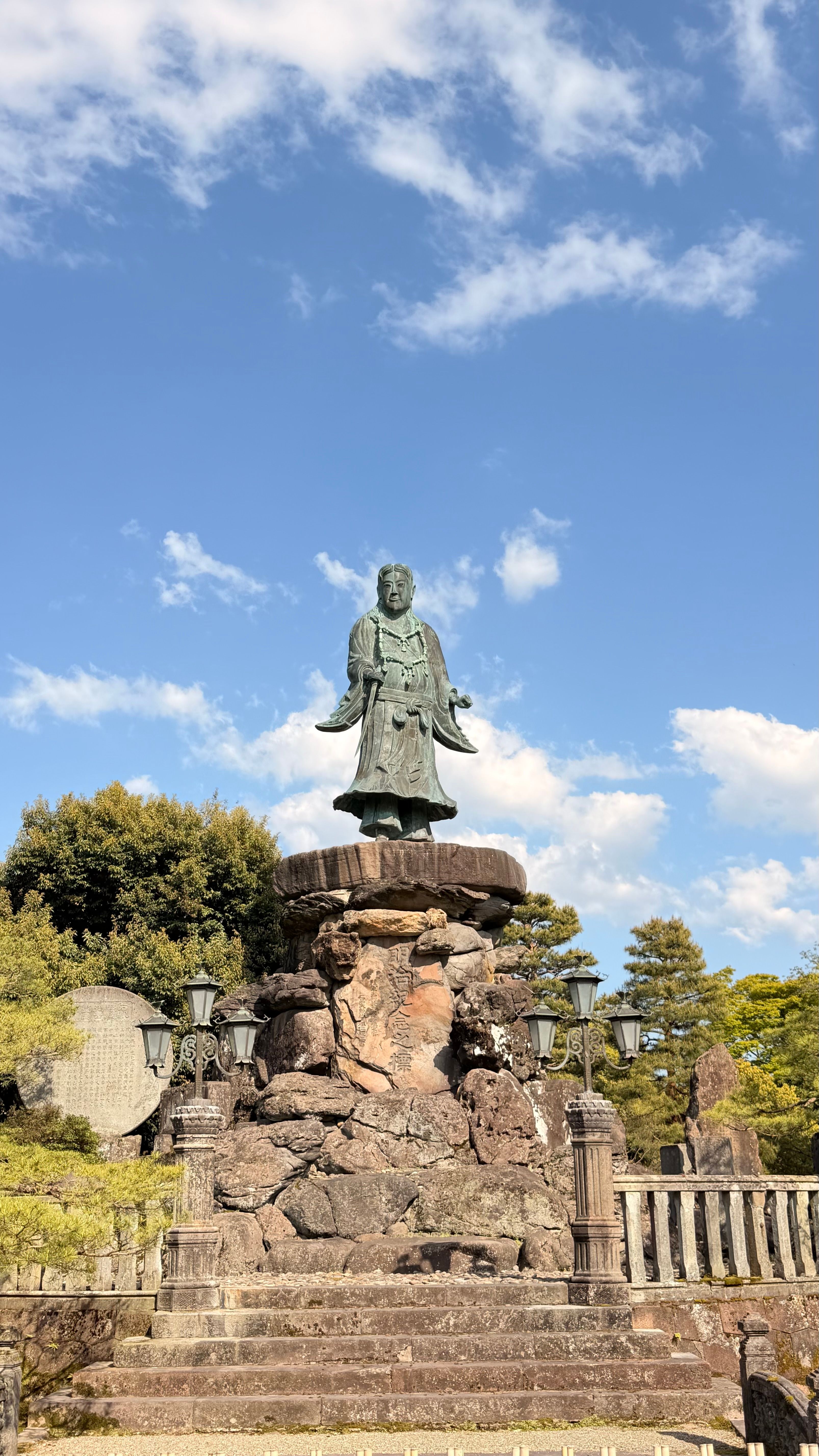 A serene statue in a Japanese garden in Kanazawa, Japan, under a clear blue sky.