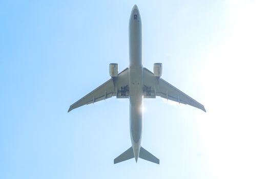A commercial airplane captured from below, soaring against a bright blue sky.
