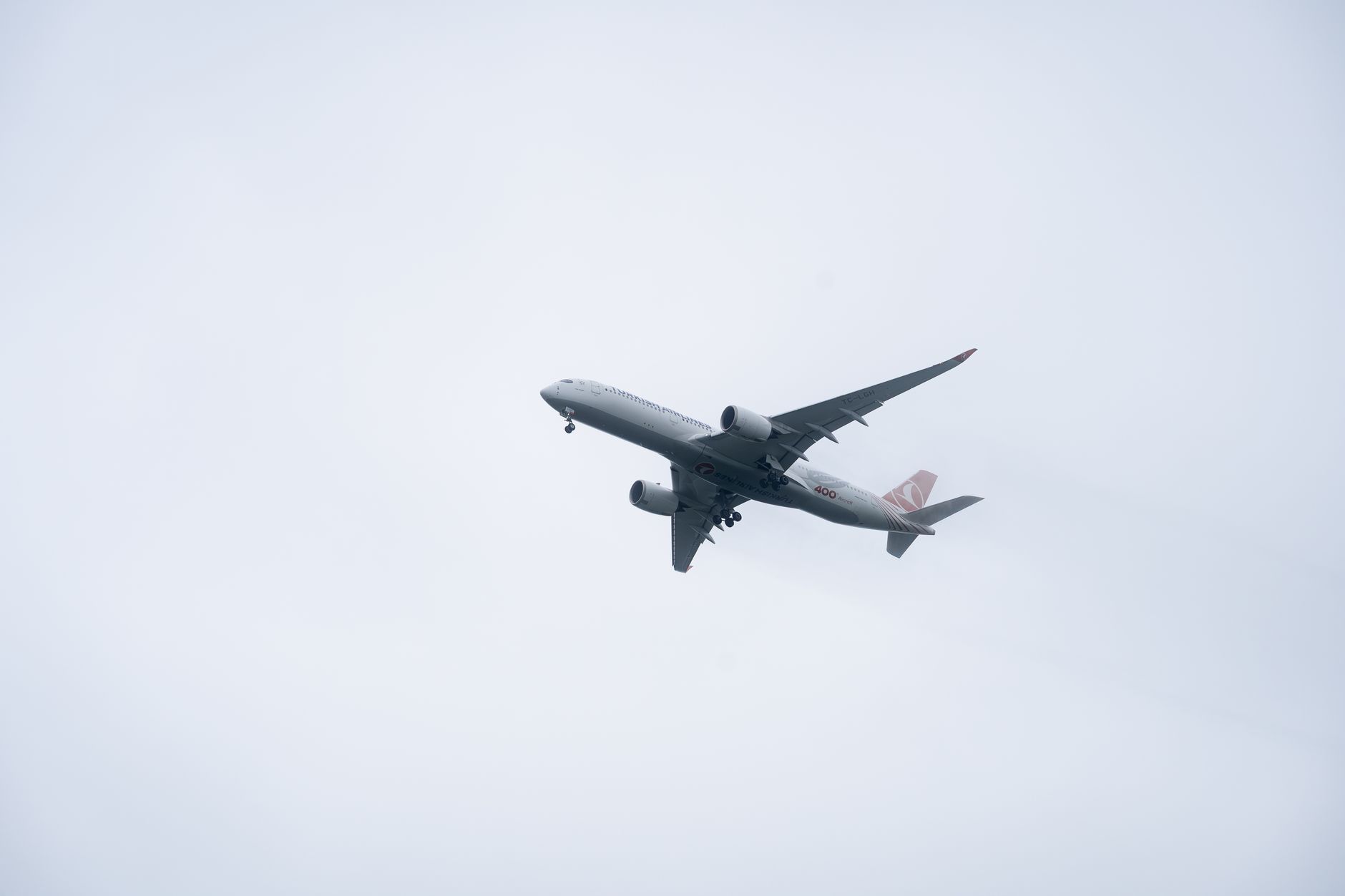 Wide-body aircraft flying high amidst overcast skies, showcasing modern air travel.