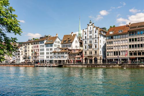 Free Scenic view of Zurich's historic waterfront buildings along the Limmat River on a sunny day. Stock Photo
