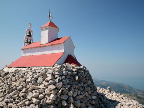 A scenic view of a small chapel on a hilltop in Montenegro with a stone base under a clear blue sky.