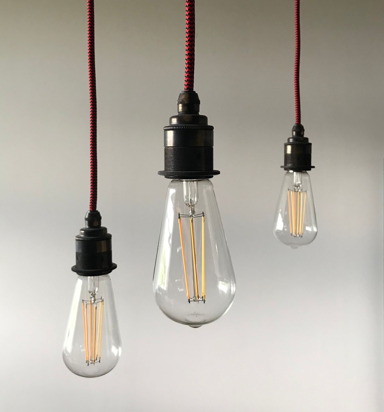 Three light bulbs hanging from cords against a bright, minimalist background