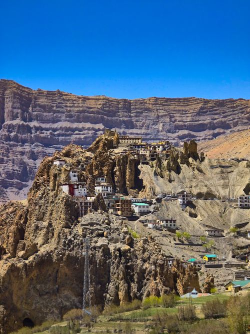 Free Stunning aerial photo of a remote mountain village set against rugged cliffs under a bright blue sky. Stock Photo
