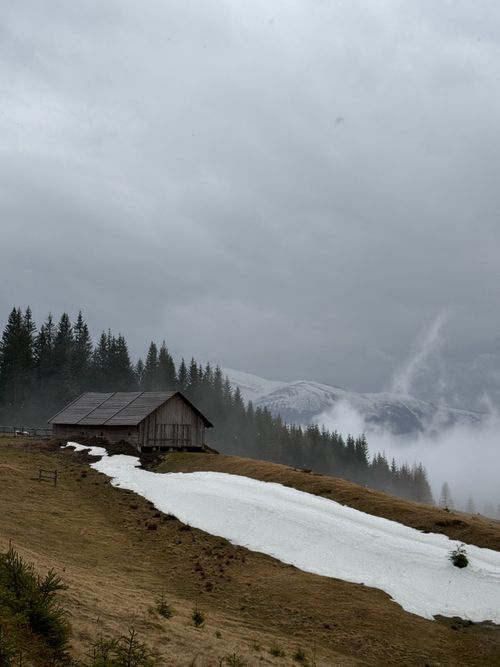 Free Mist-covered Carpathians with a rustic cabin and lingering snow, creating a tranquil winter landscape. Stock Photo